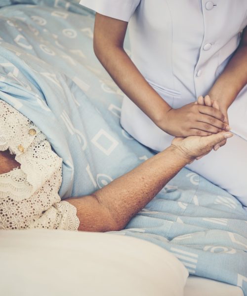 midsection-nurse-holding-hand-female-senior-patient-relaxing-bed-hospital-min